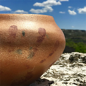 detail of micaceous clay bowl in outdoor setting with bright blue sky and clouds